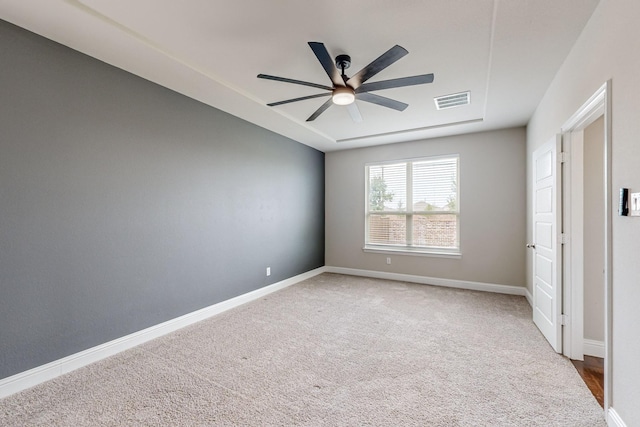 empty room featuring a raised ceiling, carpet flooring, and ceiling fan