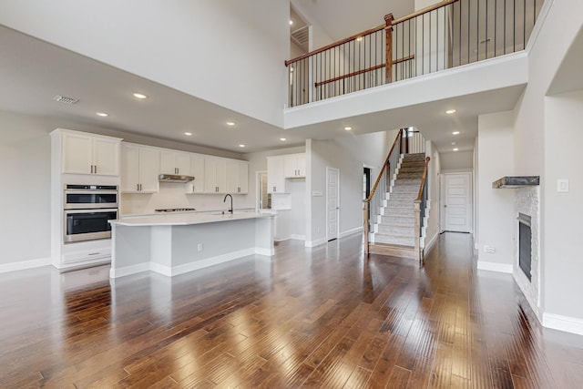 kitchen featuring double oven, dark wood-type flooring, white cabinets, and a center island with sink