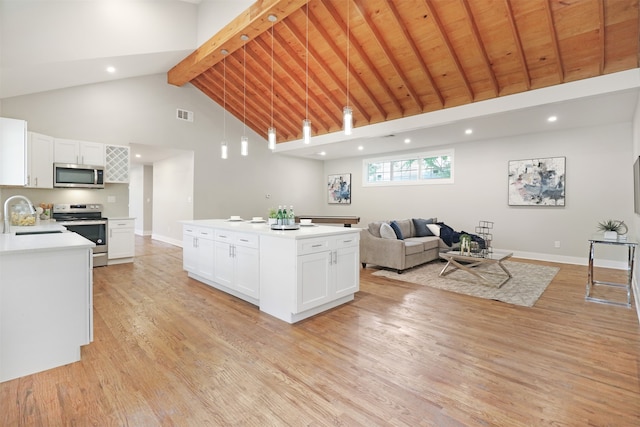 kitchen with white cabinetry, a center island, beamed ceiling, appliances with stainless steel finishes, and high vaulted ceiling