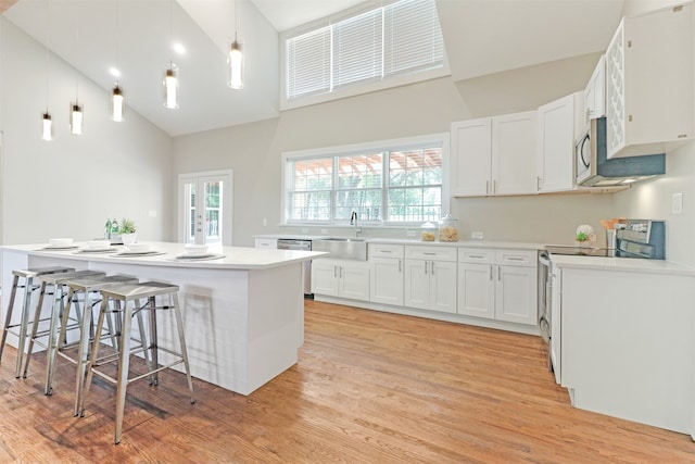 kitchen featuring a breakfast bar, light wood-type flooring, white cabinets, stainless steel appliances, and high vaulted ceiling