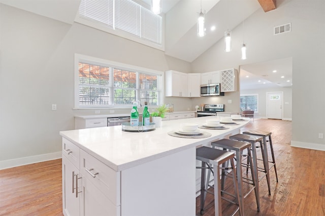 kitchen with appliances with stainless steel finishes, light hardwood / wood-style flooring, pendant lighting, a kitchen island, and high vaulted ceiling