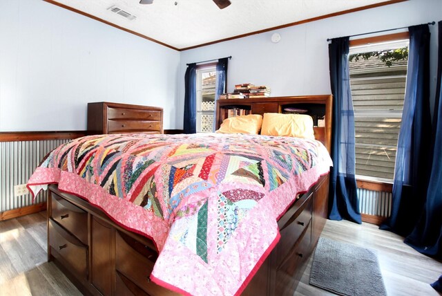 bedroom featuring ceiling fan, multiple windows, light hardwood / wood-style flooring, and ornamental molding