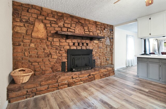 unfurnished living room with a stone fireplace, light hardwood / wood-style flooring, and a textured ceiling