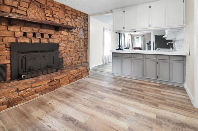 kitchen featuring a stone fireplace, light hardwood / wood-style floors, gray cabinetry, and a textured ceiling