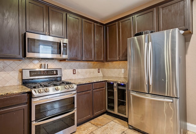 kitchen with stainless steel appliances, light stone counters, dark brown cabinets, backsplash, and light tile patterned flooring