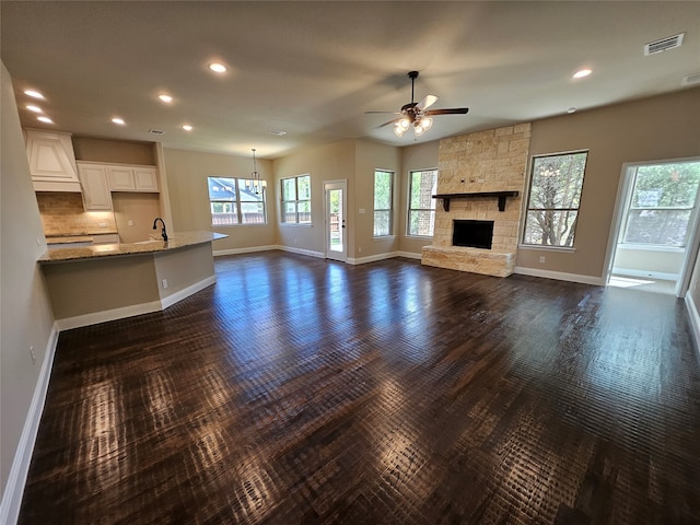 unfurnished living room with ceiling fan, a stone fireplace, sink, and dark wood-type flooring