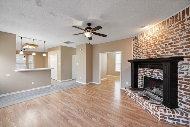 unfurnished living room featuring light hardwood / wood-style floors, a textured ceiling, a brick fireplace, and ceiling fan