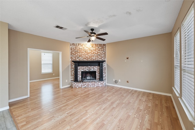 unfurnished living room featuring a textured ceiling, light hardwood / wood-style flooring, a brick fireplace, and ceiling fan