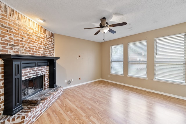 unfurnished living room with a textured ceiling, ceiling fan, light hardwood / wood-style floors, brick wall, and a fireplace