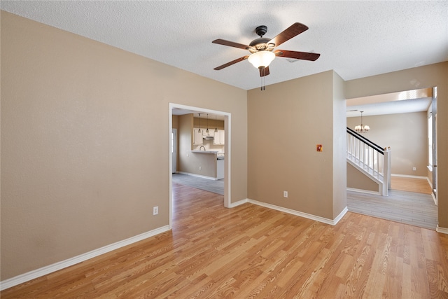 unfurnished room featuring a textured ceiling, light hardwood / wood-style flooring, and ceiling fan with notable chandelier