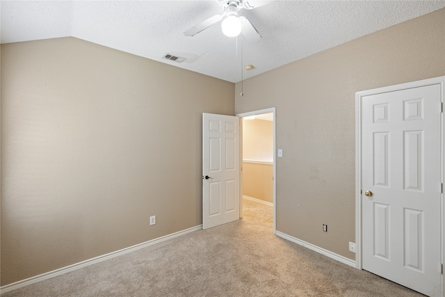 unfurnished bedroom with lofted ceiling, a textured ceiling, light colored carpet, and ceiling fan