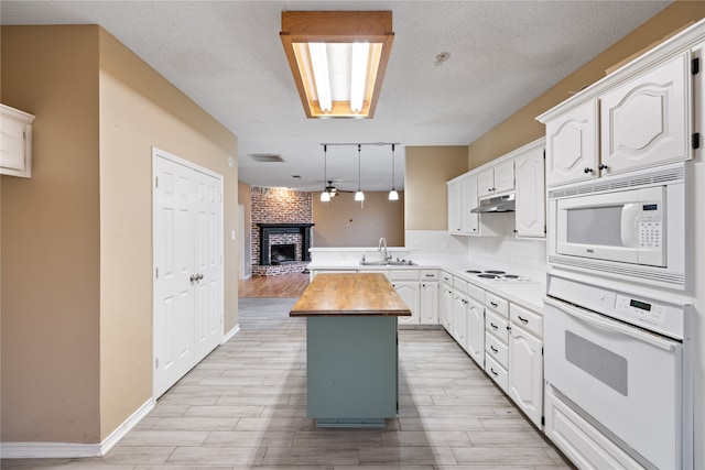 kitchen featuring white appliances, white cabinets, a center island, wood counters, and a fireplace