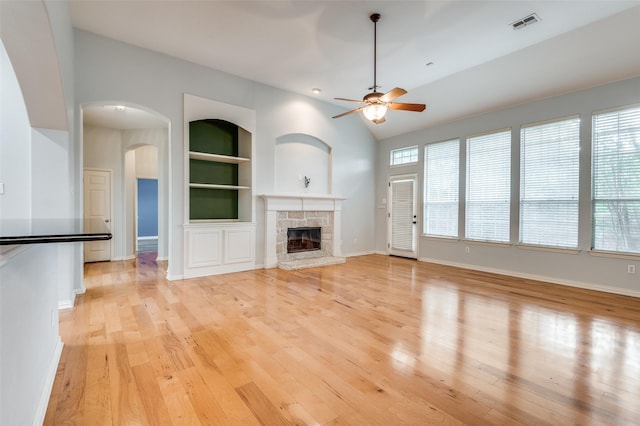 unfurnished living room featuring lofted ceiling, light hardwood / wood-style flooring, ceiling fan, a fireplace, and built in shelves