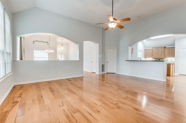 unfurnished living room featuring ceiling fan with notable chandelier, a healthy amount of sunlight, and light wood-type flooring