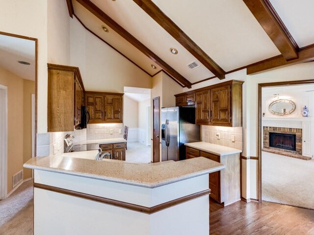 kitchen with a fireplace, wood-type flooring, beamed ceiling, stainless steel fridge, and backsplash