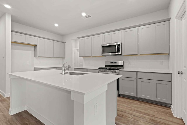 kitchen with gray cabinetry, sink, an island with sink, and appliances with stainless steel finishes