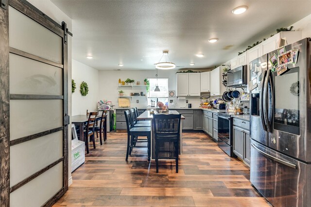 kitchen with stainless steel appliances, wood-type flooring, a barn door, and gray cabinetry