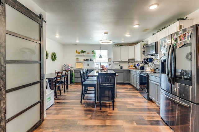 kitchen with decorative light fixtures, stainless steel appliances, a barn door, dark wood-type flooring, and white cabinets