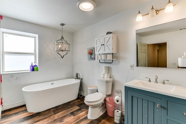 full bath with baseboards, toilet, wood finished floors, a freestanding bath, and vanity