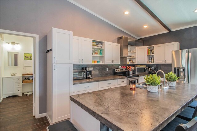 kitchen with wall chimney range hood, white cabinets, appliances with stainless steel finishes, a kitchen breakfast bar, and backsplash