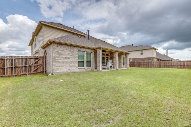 back of house with a shingled roof, a lawn, a fenced backyard, a patio area, and brick siding