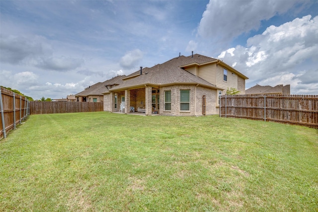 back of house featuring a yard, brick siding, a shingled roof, and a fenced backyard