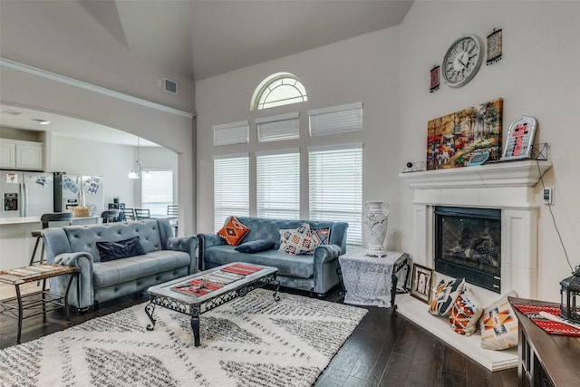 living area featuring arched walkways, dark wood-style flooring, visible vents, a fireplace with raised hearth, and a high ceiling