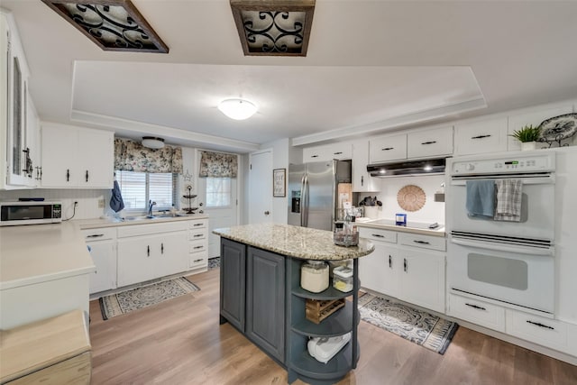 kitchen with a center island, a raised ceiling, white appliances, light hardwood / wood-style floors, and white cabinets