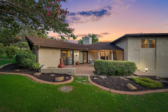 back house at dusk featuring a lawn