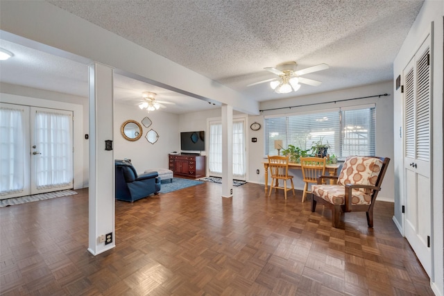 living area with french doors, ceiling fan, dark parquet floors, and a textured ceiling