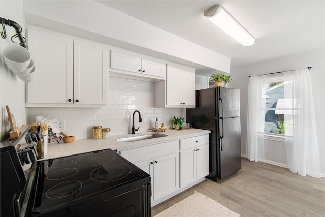 kitchen with light wood-type flooring, stainless steel electric stove, decorative backsplash, sink, and black fridge