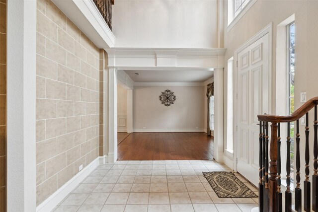 entryway featuring tile walls, light hardwood / wood-style flooring, ornamental molding, and a towering ceiling