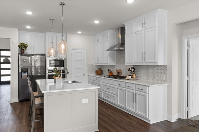 kitchen featuring wall chimney range hood, sink, an island with sink, and white cabinets