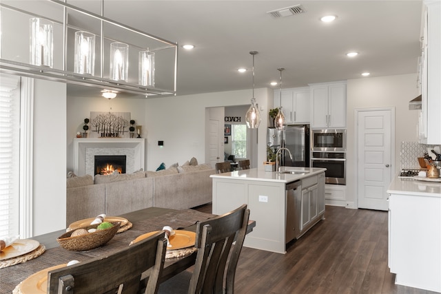 kitchen with pendant lighting, stainless steel appliances, a center island with sink, and white cabinets