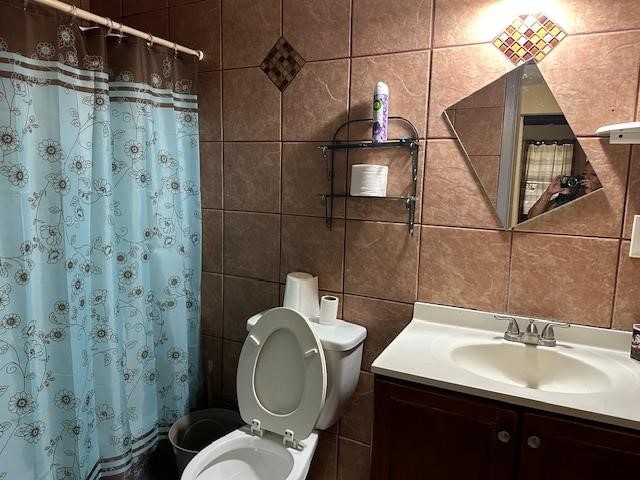 bathroom featuring vanity, toilet, and tile walls