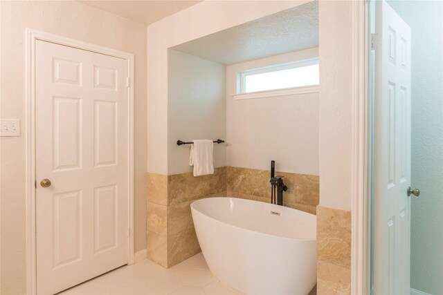 bathroom with a tub to relax in, tile patterned flooring, and tile walls