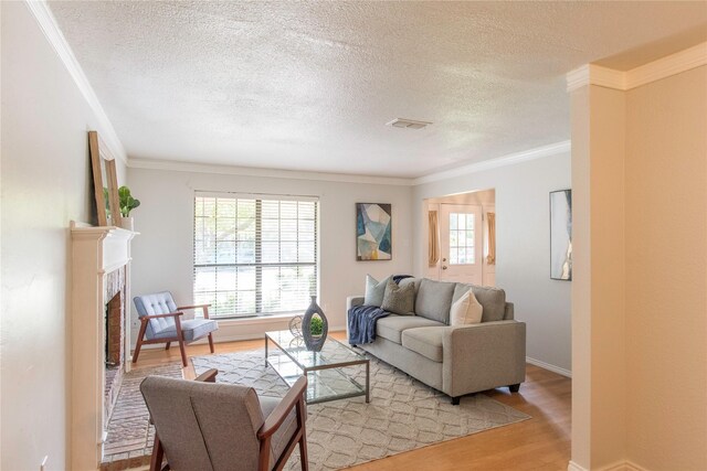 living room featuring a fireplace, a textured ceiling, light hardwood / wood-style floors, and ornamental molding