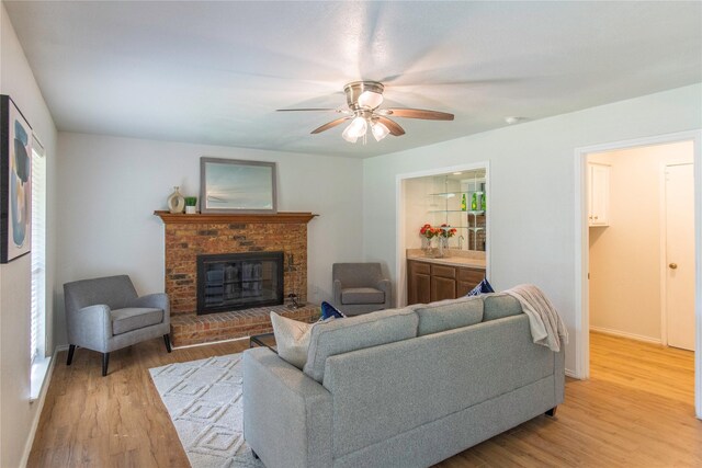 living room with a fireplace, a wealth of natural light, light wood-type flooring, and ceiling fan