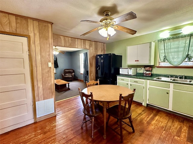 kitchen featuring ceiling fan, dark hardwood / wood-style flooring, sink, wooden walls, and black refrigerator with ice dispenser