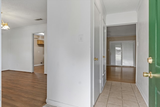 hallway with crown molding, light wood-type flooring, and a textured ceiling