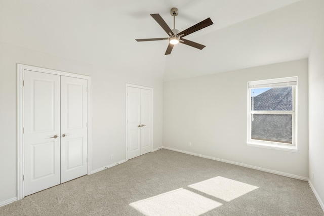 unfurnished bedroom with multiple closets, lofted ceiling, light colored carpet, and ceiling fan