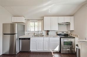 kitchen with appliances with stainless steel finishes, dark hardwood / wood-style flooring, and white cabinetry