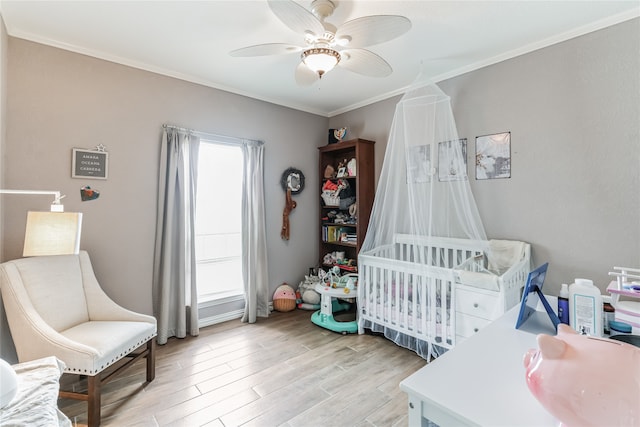 bedroom with crown molding, light hardwood / wood-style flooring, ceiling fan, and a nursery area