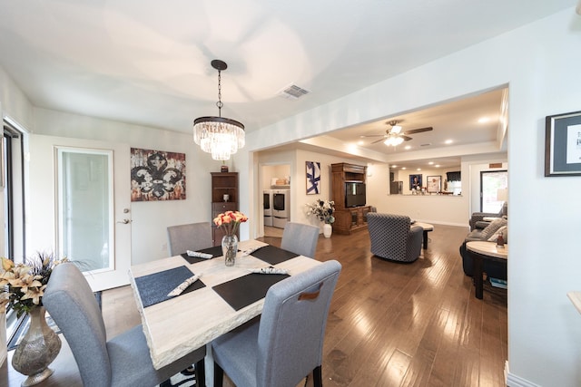 dining room with a raised ceiling, dark wood-type flooring, ceiling fan with notable chandelier, and washer and clothes dryer