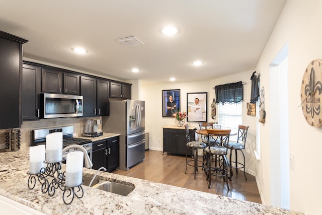 kitchen featuring appliances with stainless steel finishes, light wood-type flooring, light stone counters, and decorative backsplash