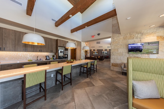 kitchen with a breakfast bar, decorative light fixtures, decorative backsplash, dark brown cabinetry, and beam ceiling