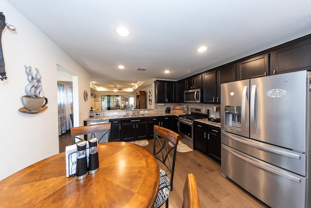 kitchen with sink, kitchen peninsula, stainless steel appliances, light hardwood / wood-style floors, and decorative backsplash