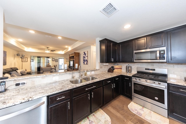 kitchen with sink, tasteful backsplash, light wood-type flooring, appliances with stainless steel finishes, and a raised ceiling