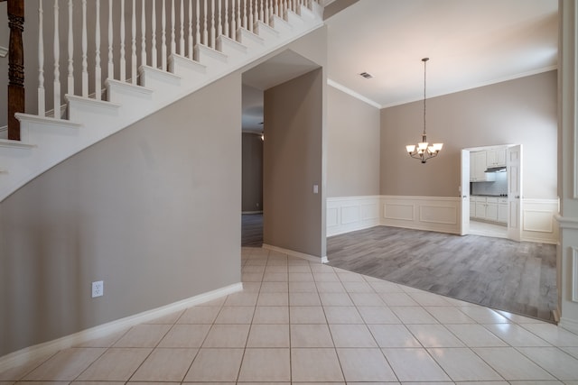 spare room featuring ornamental molding, an inviting chandelier, light wood-type flooring, and a high ceiling