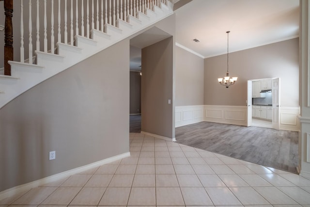 unfurnished room with a high ceiling, crown molding, a chandelier, and light tile patterned flooring